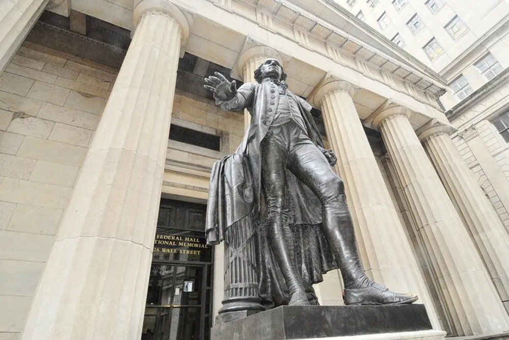 A statue of a historical figure stands prominently before the entrance of the Federal Hall National Memorial on Wall Street
