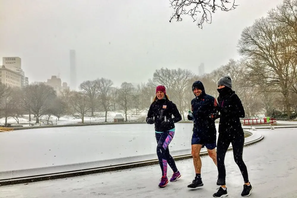 Three people are jogging together in a winter setting with snow falling around them