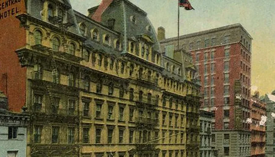 The image shows a vintage color postcard depicting a densely built urban street scene with ornate architecture from an earlier period, showcasing a multi-story building with a flag proudly displayed on the facade.