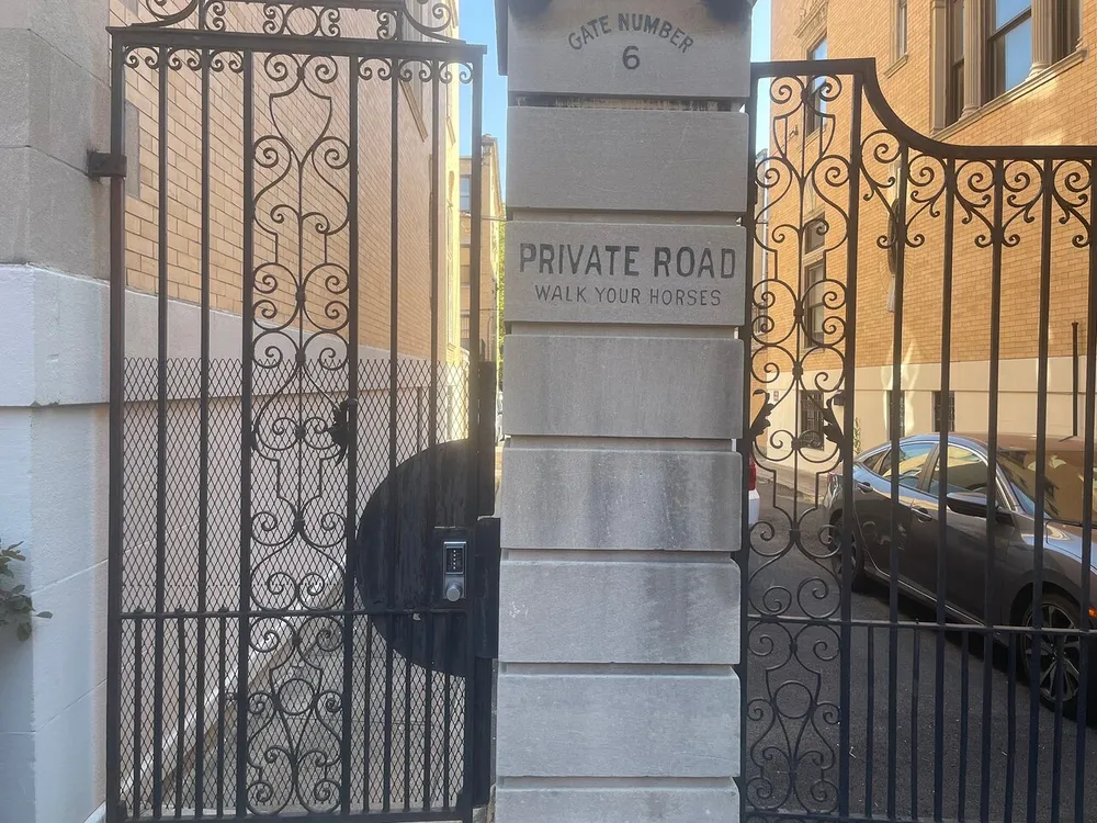This image shows an ornate black iron gate with a sign that reads PRIVATE ROAD WALK YOUR HORSES next to a stone pillar indicating GATE NUMBER 6