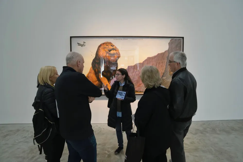 A group of people are engaged in a discussion in front of a large framed artwork featuring a lion in a gallery setting