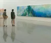 Three individuals are standing in an art gallery observing a large colorful abstract painting