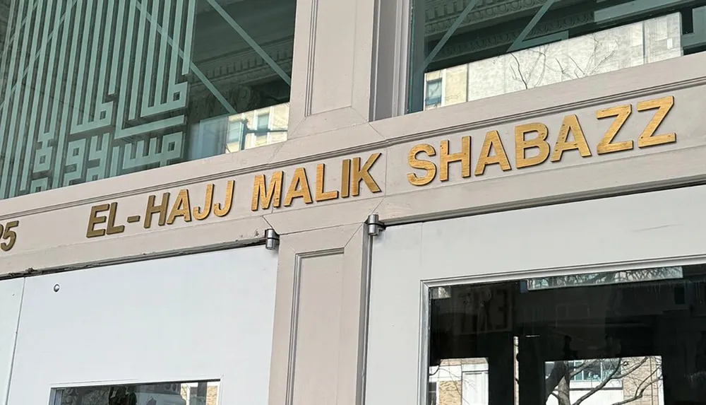 The image shows a building faade with the name EL-HAJJ MALIK SHABAZZ in bold gold-colored letters above the entrance