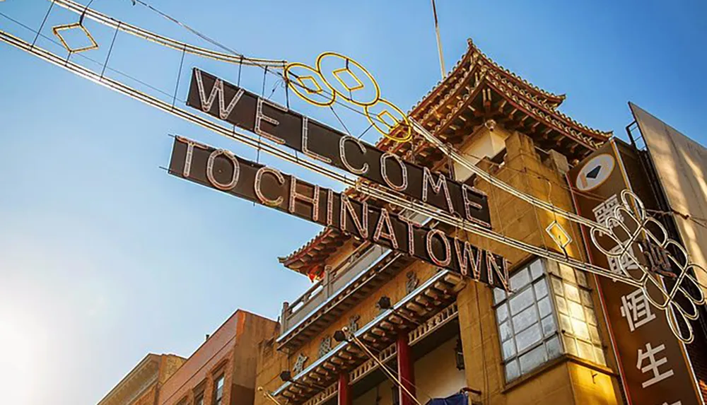 An elaborate gateway with an illuminated Welcome to Chinatown sign and decorative elements in a city setting under a clear sky