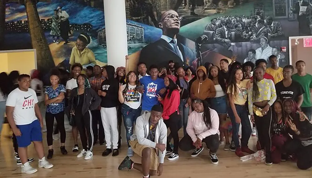 A group of students poses for a photo in a room with vibrant murals depicting African American history and culture