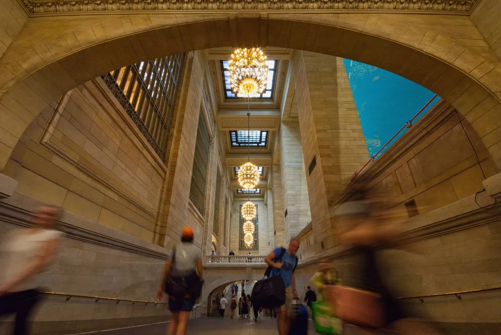 The image shows a bustling corridor with people in motion elegant chandeliers and grand architecture likely in a historic train station or public building