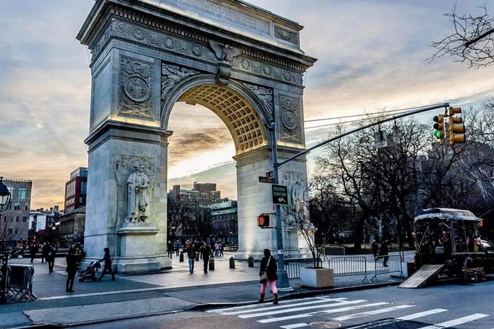 The image features the iconic Washington Square Arch in New York City with people crossing the street and walking around the park at twilight
