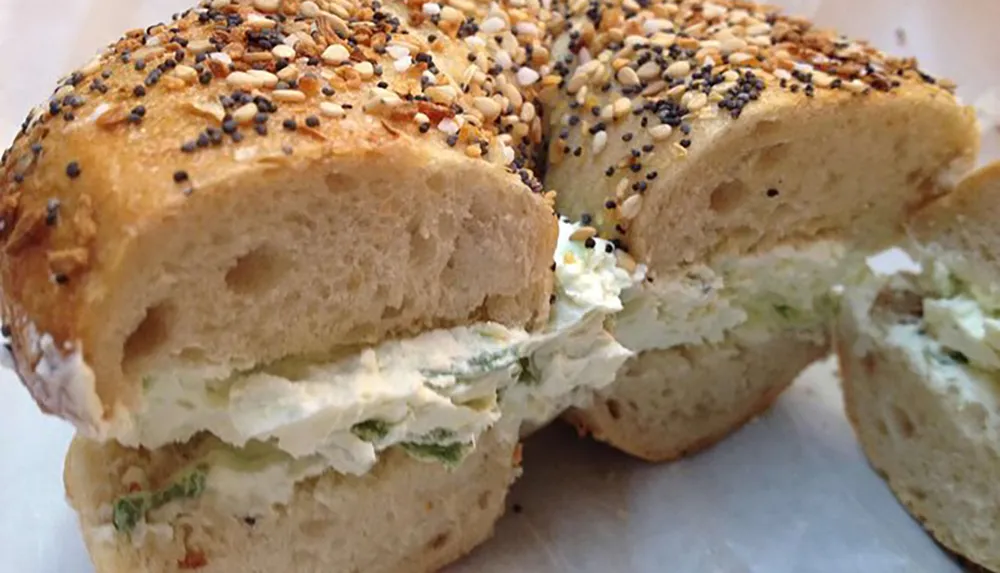 A bagel with cream cheese and a topping of various seeds cut in half is displayed