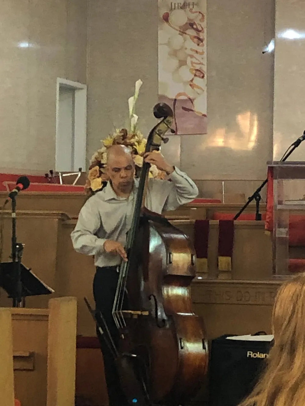 A person is playing a double bass in a room with a religious banner in the background