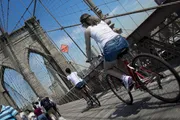 Cyclists and pedestrians share the pathway on the Brooklyn Bridge under a sunny sky.