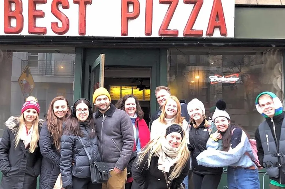 A group of smiling people are posing for a photo in front of an establishment with a sign that reads BEST PIZZA
