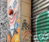 The image shows an urban wall with a vibrant clown graffiti artwork alongside various tags and a partially visible metal shutter