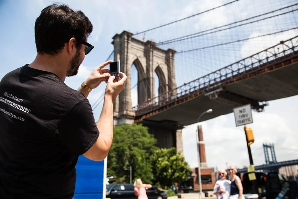 A person is taking a photo with a smartphone of the Brooklyn Bridge on a sunny day
