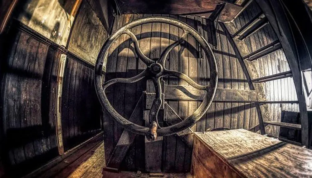 The image shows a large old-fashioned steering wheel inside the wooden interior of what appears to be the captains bridge of a vintage ship