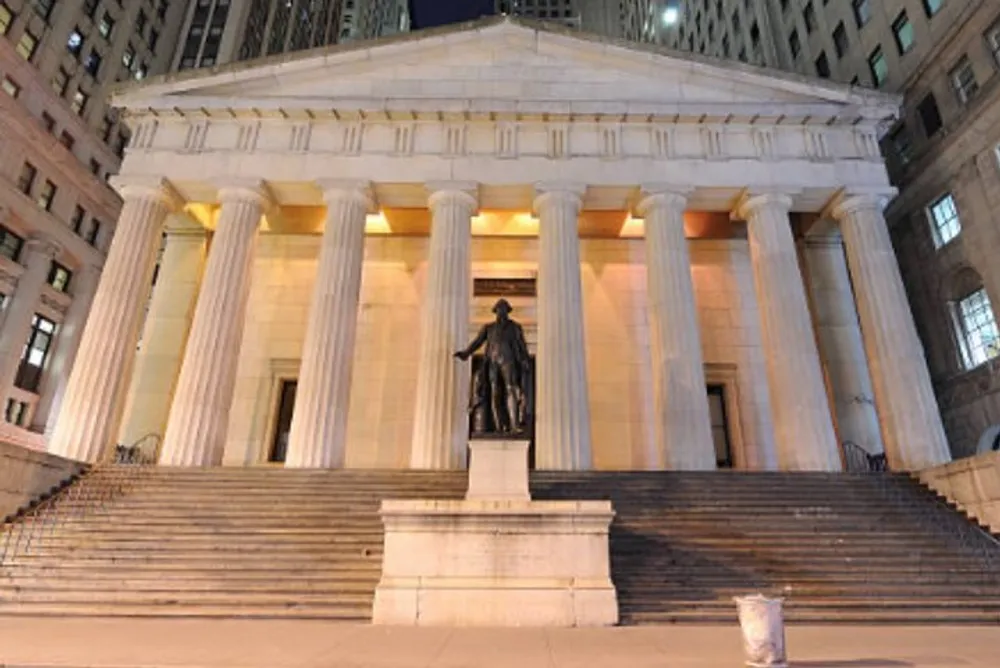 The image shows a grand neoclassical building with columns at night prominently featuring a statue in front of its large staircase