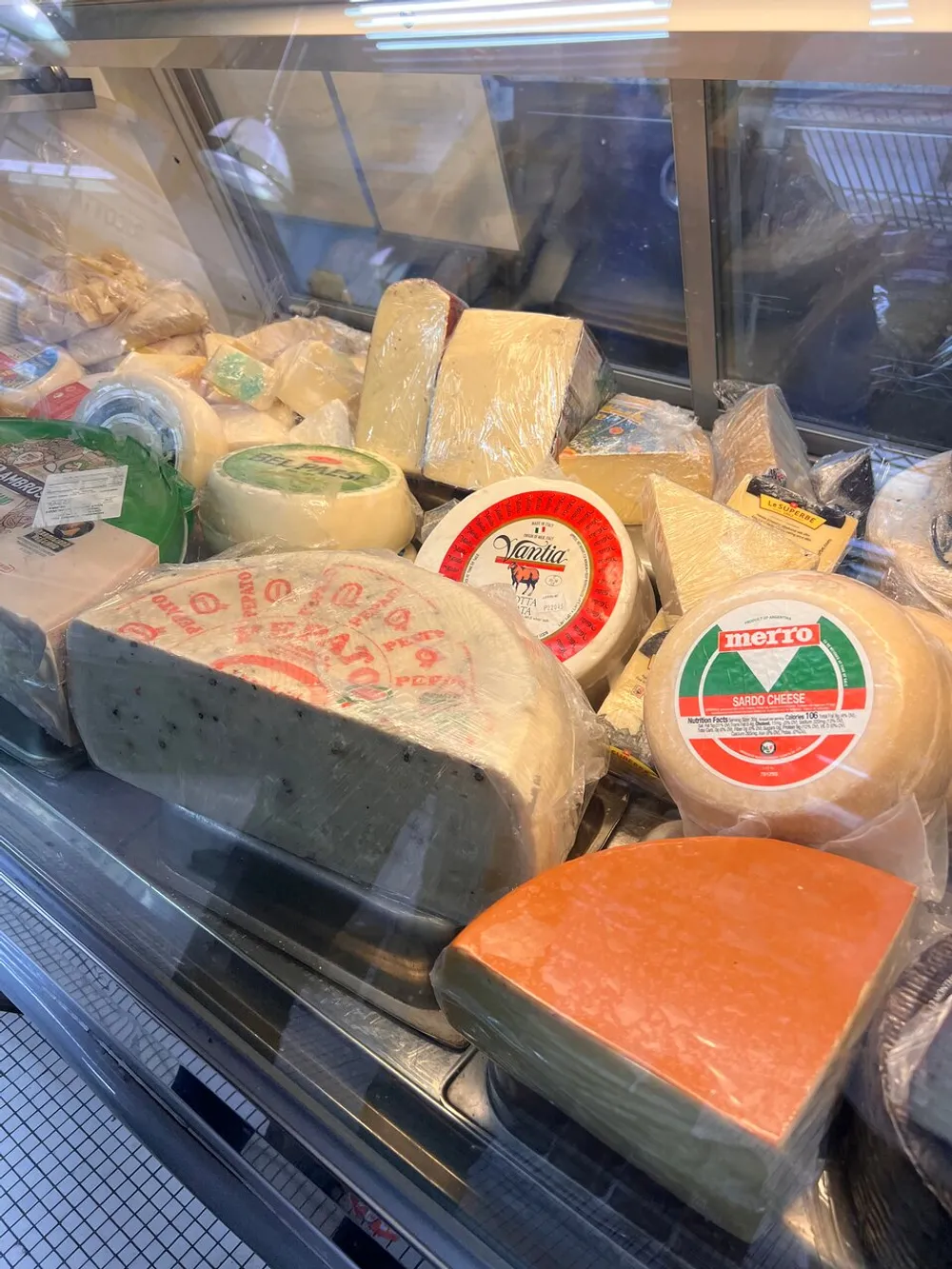The image shows a variety of cheeses displayed in a refrigerated deli case