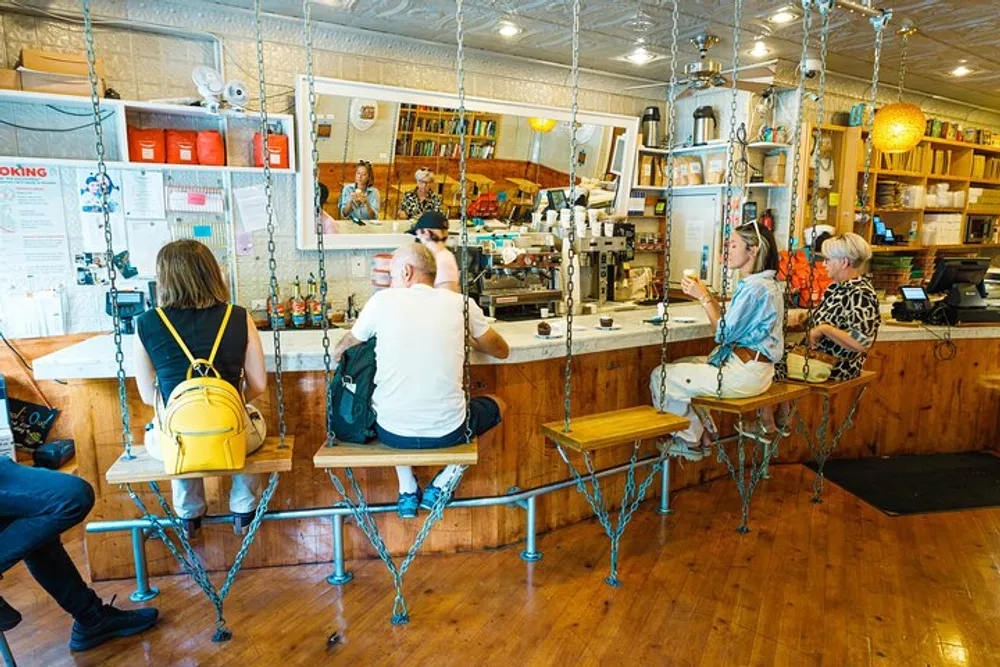 This image shows a group of customers seated on unique swing-like bar stools at a coffee shop counter while a barista works in the background