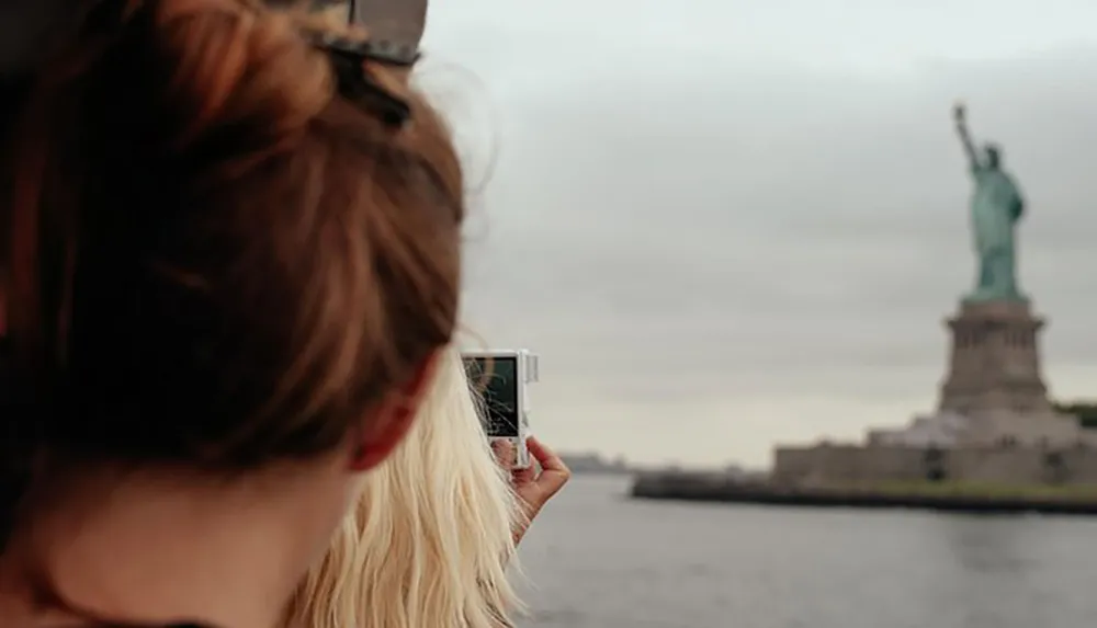 A person is photographing the Statue of Liberty with a smartphone