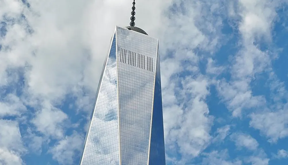 The image shows the towering One World Trade Center set against a backdrop of a partly cloudy sky