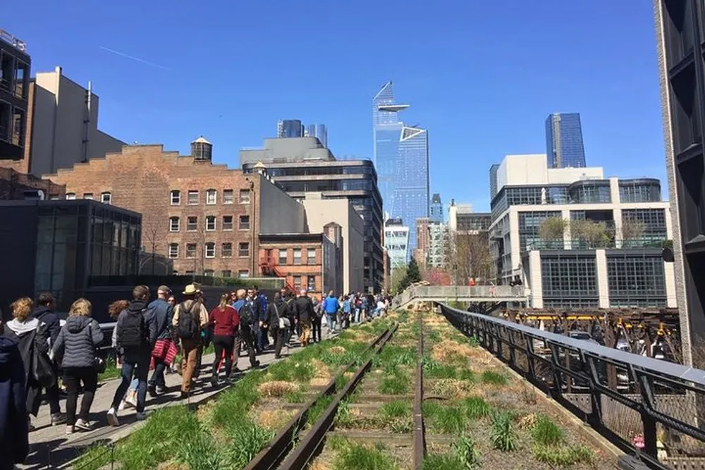 A group of people are walking along an urban park built on old elevated railroad tracks with city buildings in the background