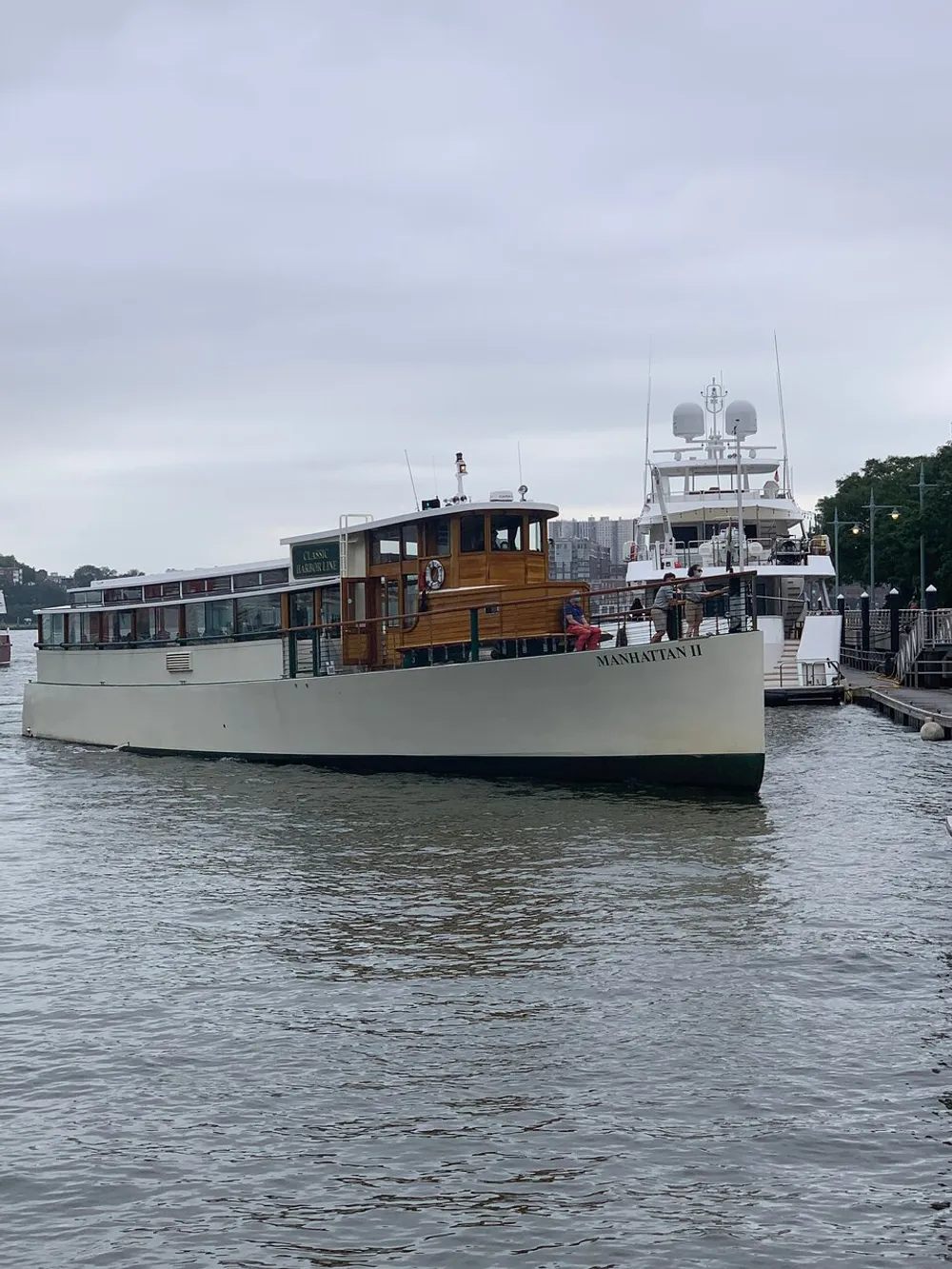 The image features a boat named Manhattan II docked at a harbor on an overcast day