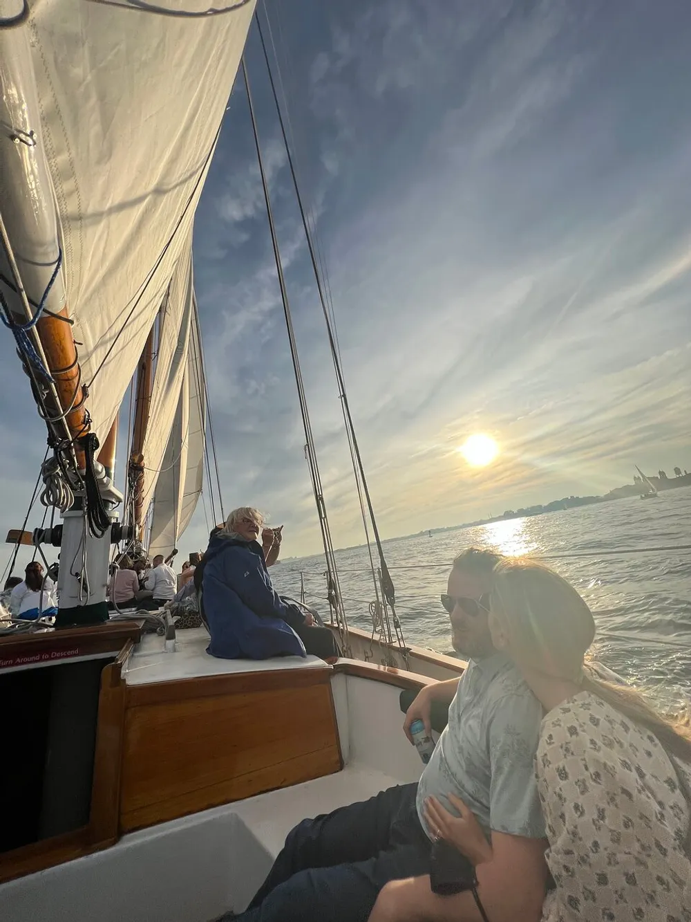 People are enjoying a serene sailboat ride at sunset with the sails hoisted against the backdrop of a calm sea and the setting sun