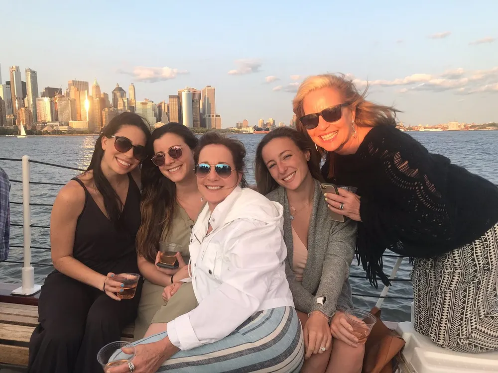 A group of happy women posing for a photo on a boat with a city skyline in the background during sunset