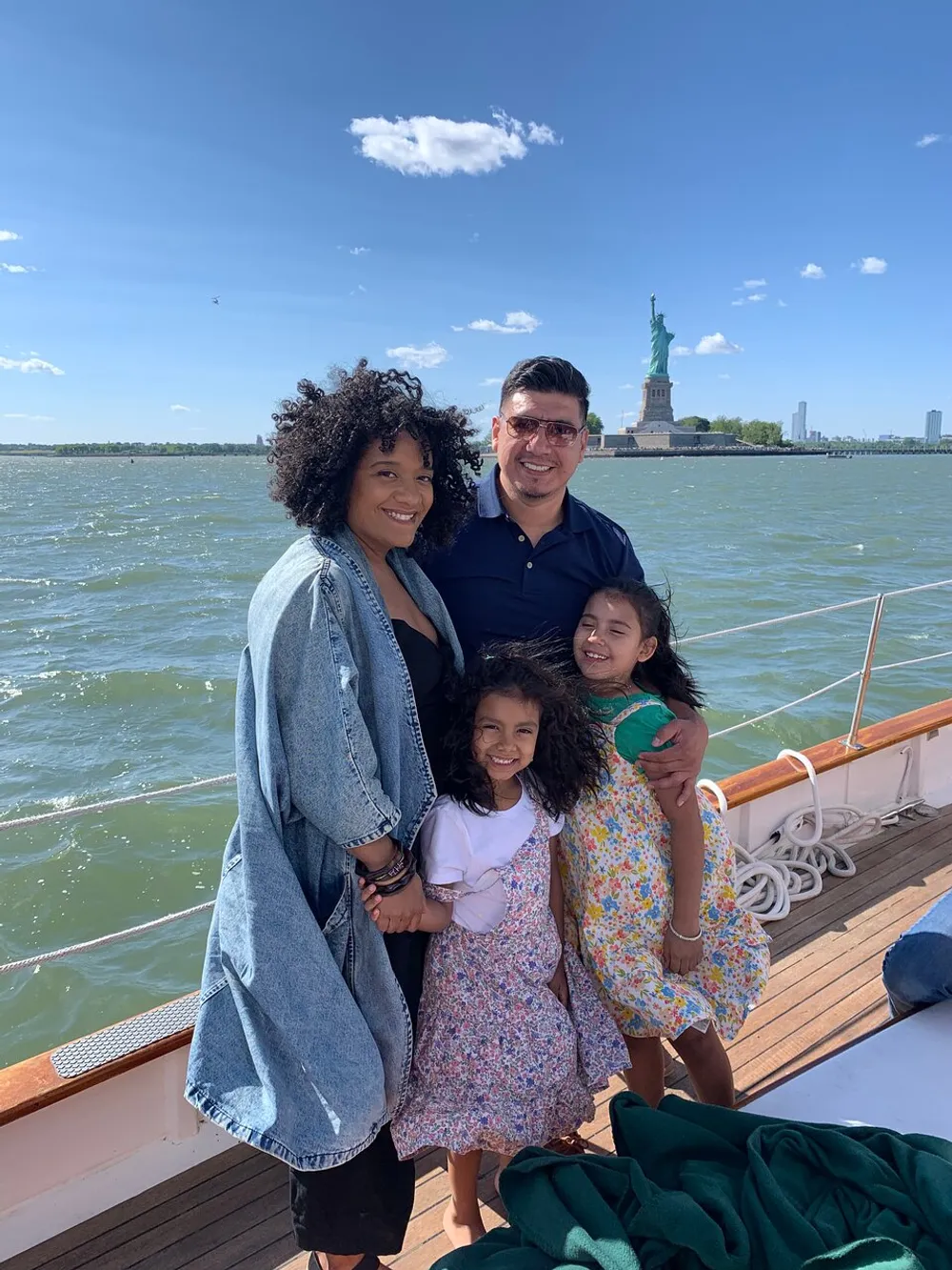 A happy family is posing for a photo on a boat with the Statue of Liberty in the background on a sunny day