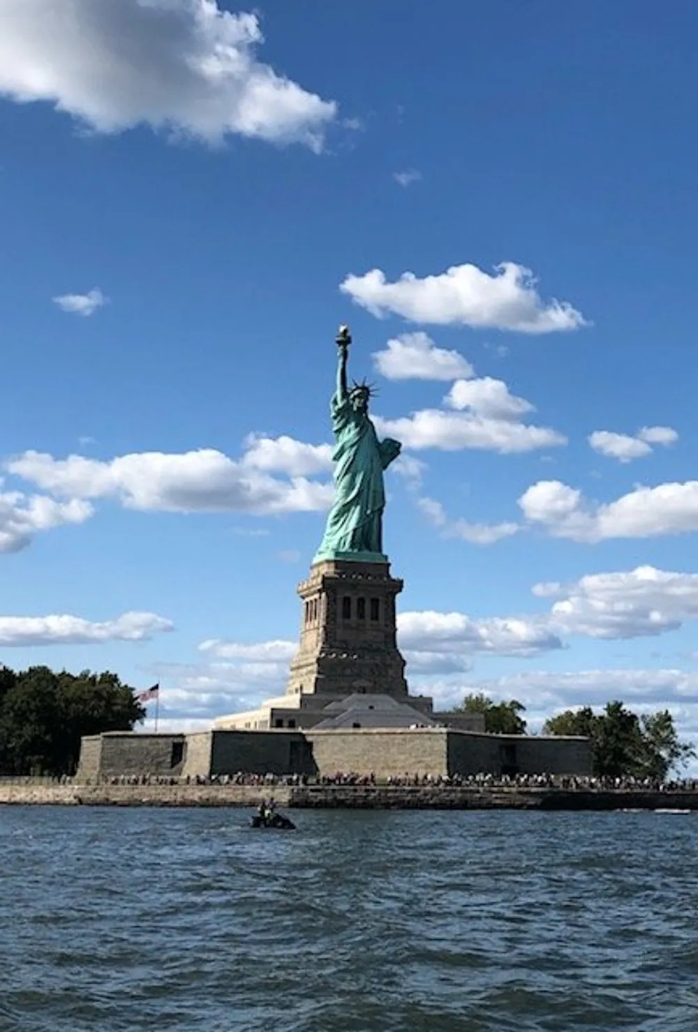 The image features the Statue of Liberty under a partly cloudy sky with views of the water in the foreground