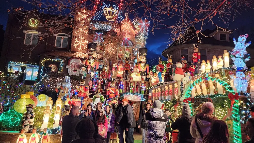 A group of people gathers in front of an elaborately decorated house with an abundance of colorful Christmas lights and festive ornaments creating a vibrant holiday atmosphere