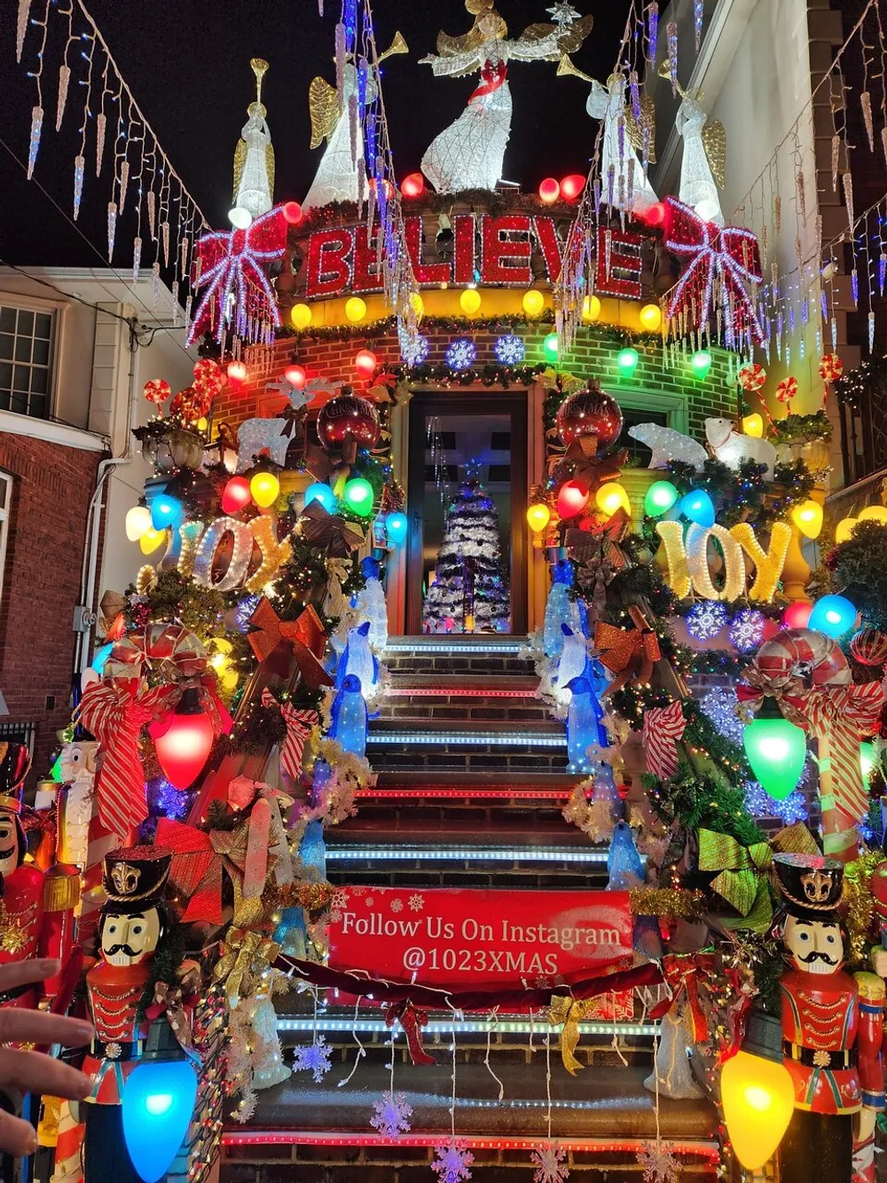 The image shows a brightly lit and festively decorated staircase with oversized Christmas ornaments nutcracker soldiers and the words BELIEVE and JOY conveying a vibrant holiday spirit