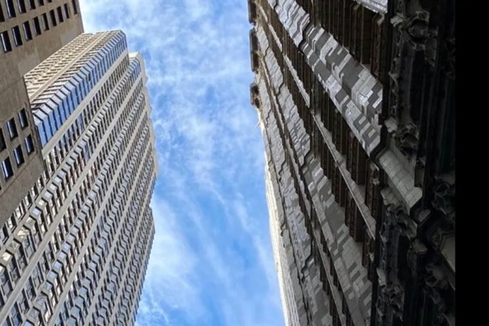 The image shows a view looking up between two contrasting styles of skyscrapers into a blue sky illustrating the architectural diversity of a citys skyline