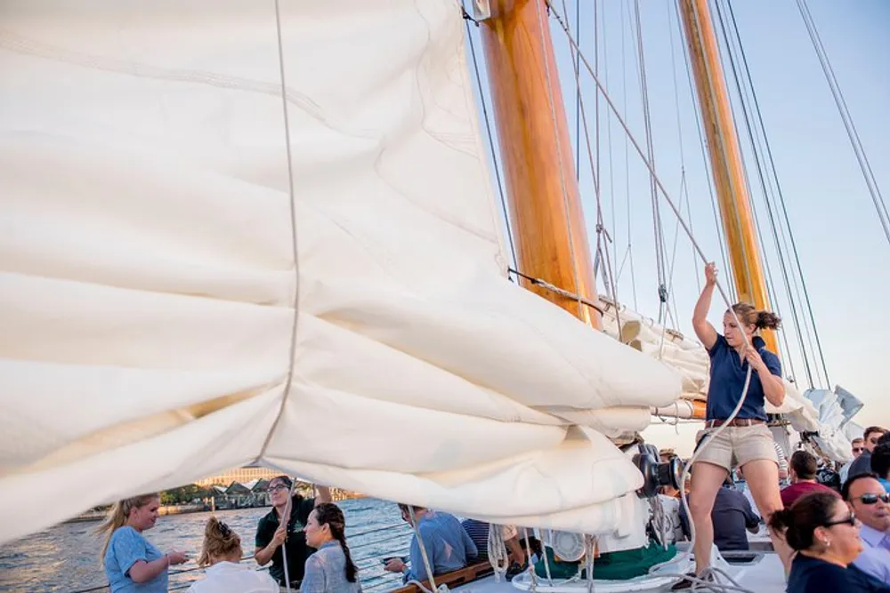 A group of people are enjoying a sailing experience on a sailboat with one person actively participating in adjusting the sails