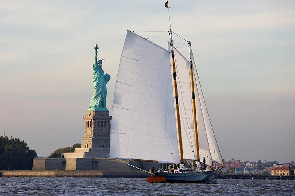 A sailboat is passing by the Statue of Liberty on a calm day