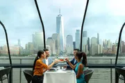 Four individuals are enjoying a meal at a dining table with a panoramic view of a city skyline in the background.