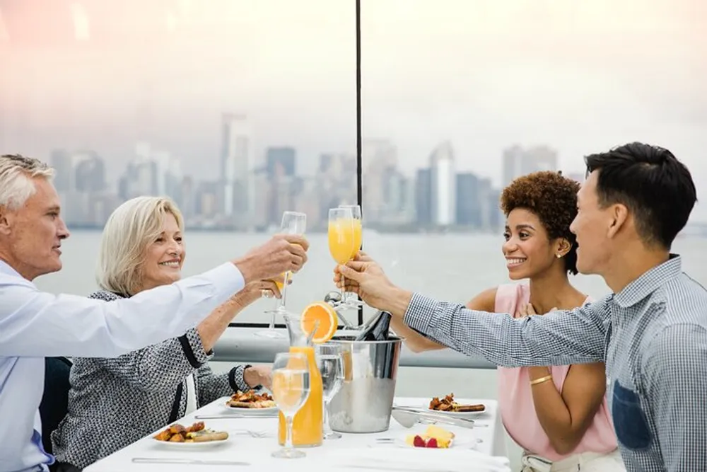 Four people are toasting with drinks at a table with a city skyline in the background