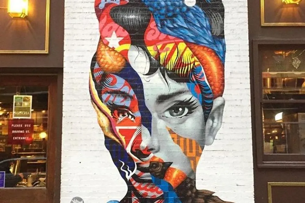 The image shows a vibrant multicolored mural of a womans face painted on an urban building wall combining elements of different patterns and styles