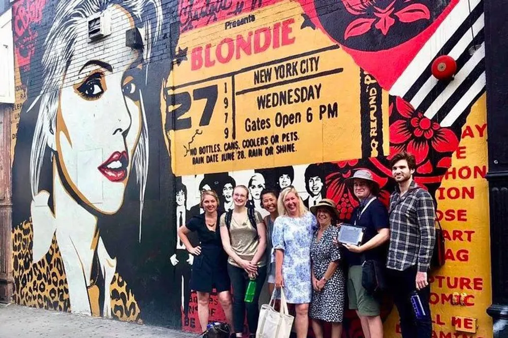 A group of people is smiling for the camera in front of a vibrant street mural advertising a Blondie concert in New York City
