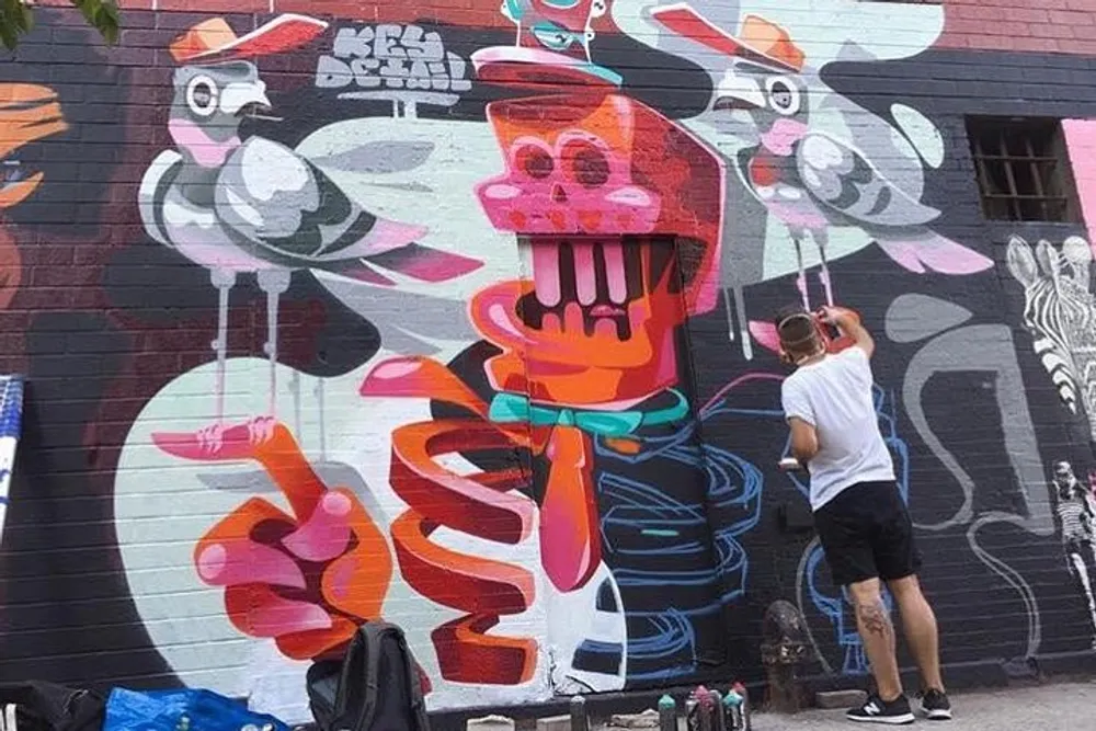 An artist is spray painting a colorful mural with abstract and playful characters on a wall