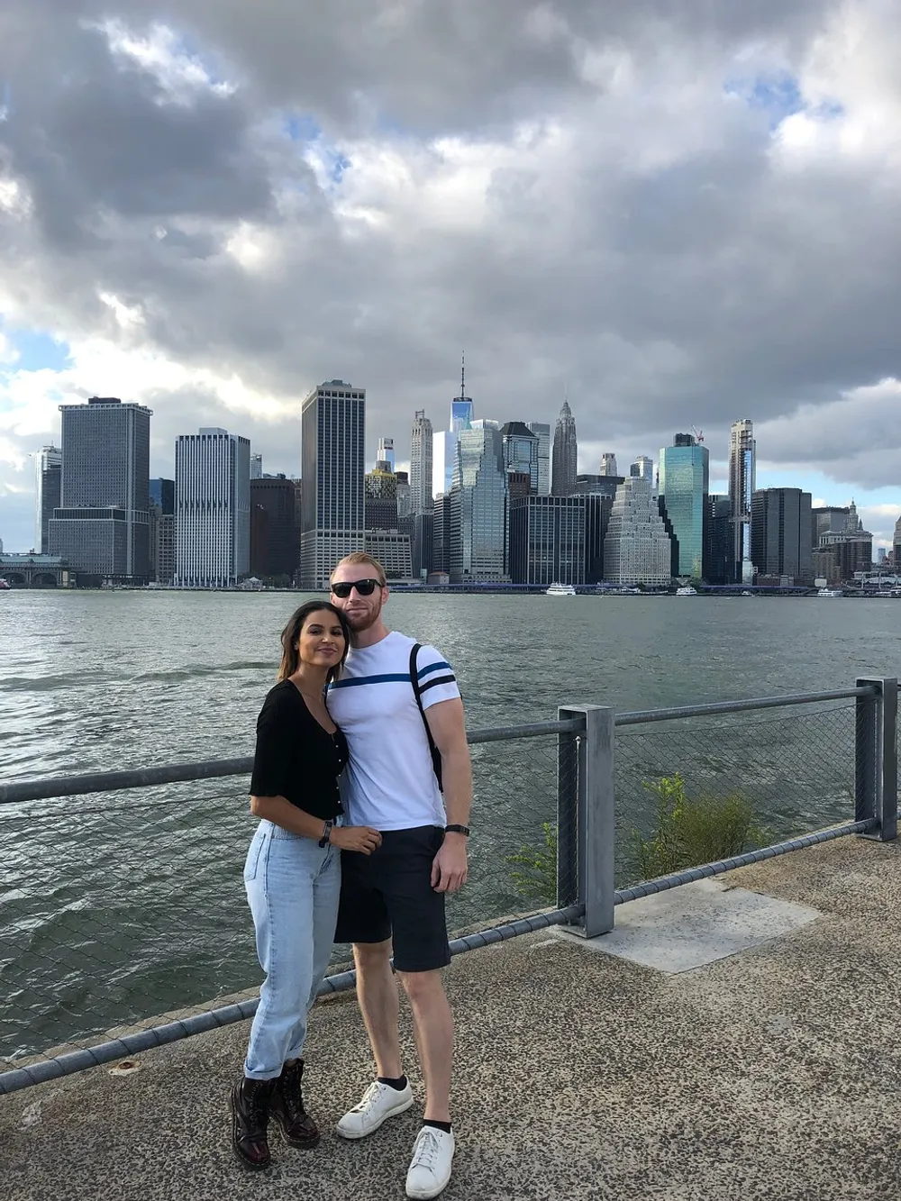 A couple is posing for a photo with the New York City skyline in the background