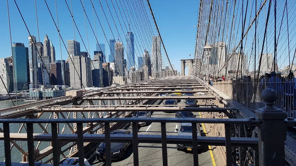 This image captures a bustling Brooklyn Bridge with pedestrian walkway and vehicular lanes set against a backdrop of the New York City skyline on a clear day