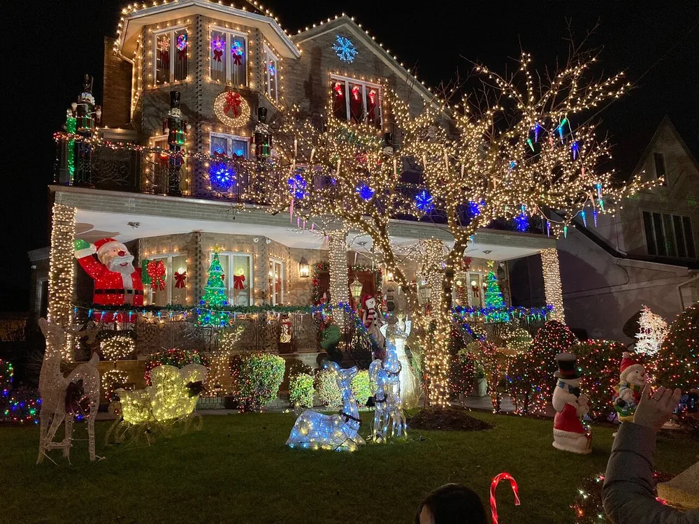 The image shows a house elaborately decorated with various colorful Christmas lights inflatable decorations and illuminated figures creating a festive night-time display