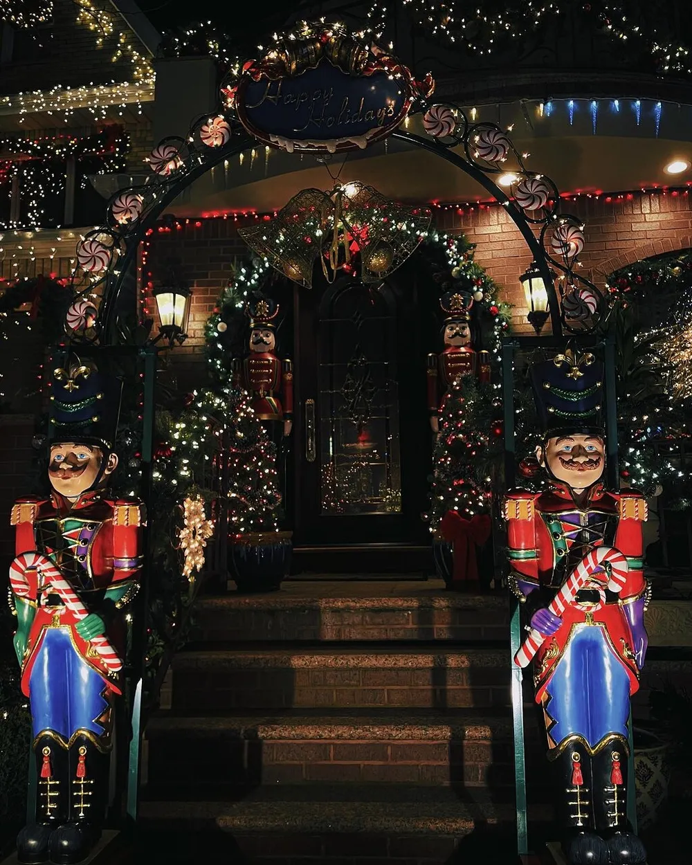 The image shows a festive holiday decoration with lit nutcracker statues flanking a staircase twinkling lights wreaths and a sign saying Happy Holidays