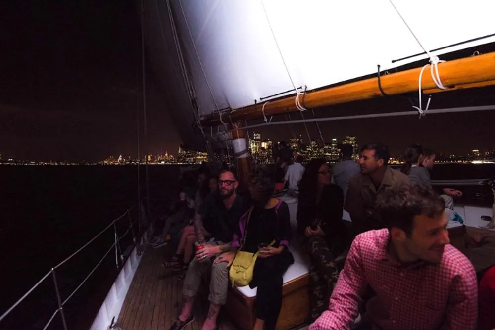 Passengers are enjoying a nighttime sailing excursion with a city skyline illuminated in the background