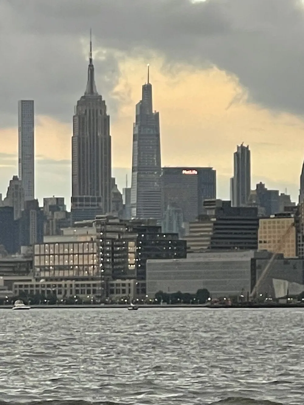The image captures a cloudy sky over a city skyline with iconic skyscrapers viewed from across a body of water