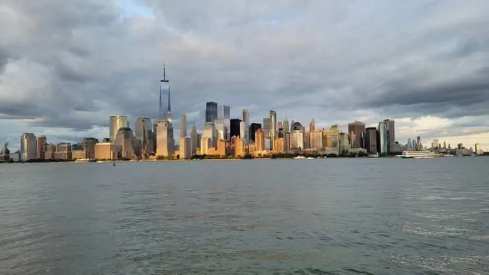 The image shows a view of a city skyline with tall buildings possibly New York City as seen from a body of water under a partly cloudy sky