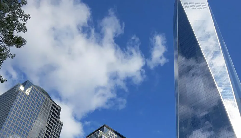 The image shows a view looking up at a towering skyscraper with a reflective facade set against a backdrop of scattered clouds in a blue sky