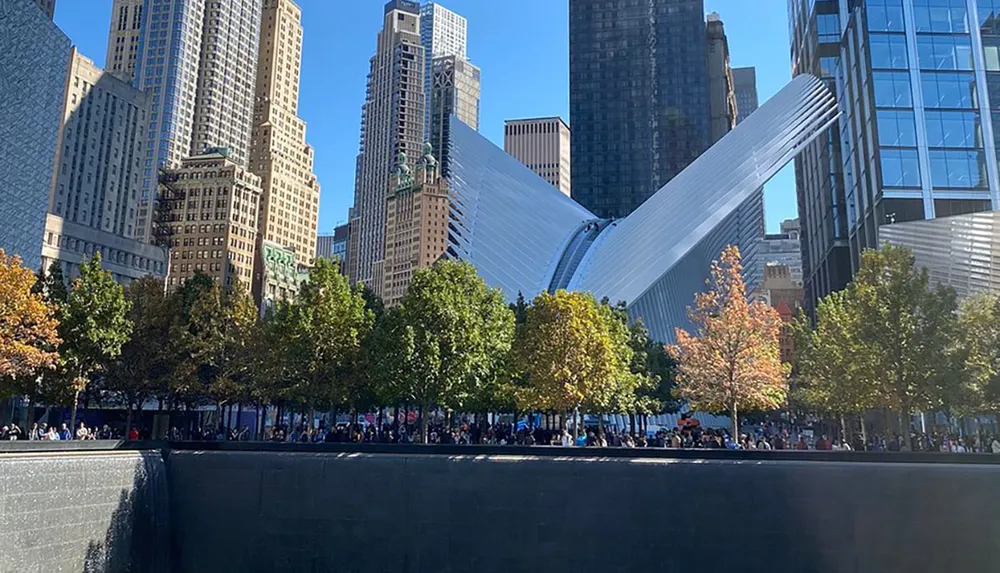 The image shows the Oculus structure at the World Trade Center site in New York City with a view of the reflecting pool of the National September 11 Memorial and surrounding skyscrapers on a clear day