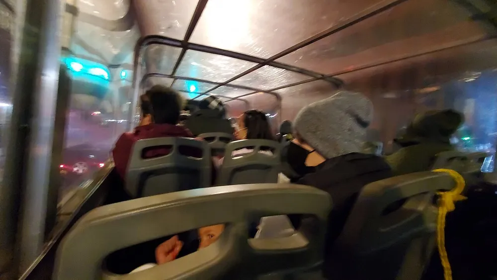 Passengers are seated in what appears to be a covered bus or trolley with transparent windows during an evening ride
