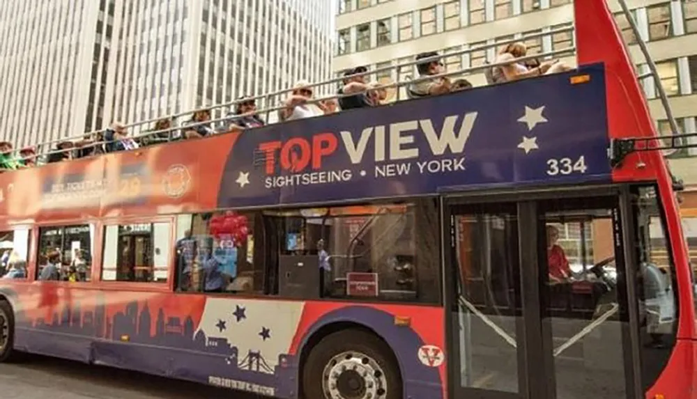This is a photo of a red double-decker sightseeing bus labeled TopView with tourists on the upper deck located in New York City